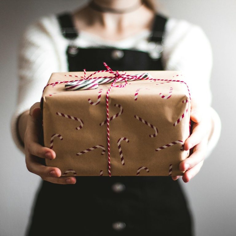 Person holding a gift wrapped in brown paper with candy cane patterns and twine.