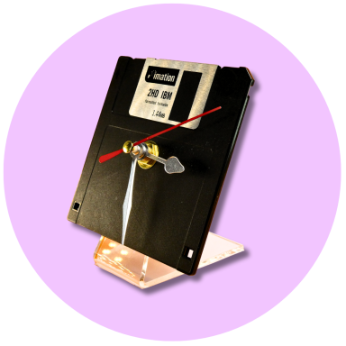 A vintage floppy disk transformed into a clock, mounted on a clear stand.